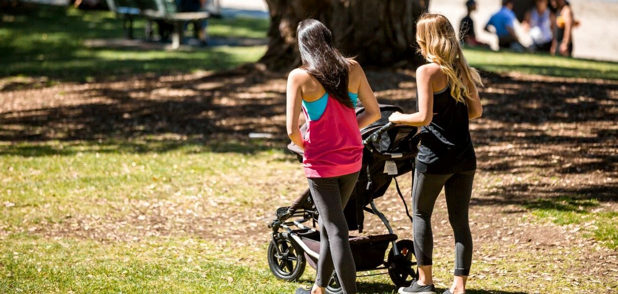 Two women walking a baby in a pram in a park