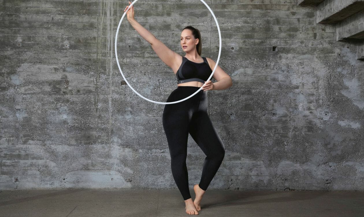 A woman wearing a Black sports bra and tights swinging a hoop.